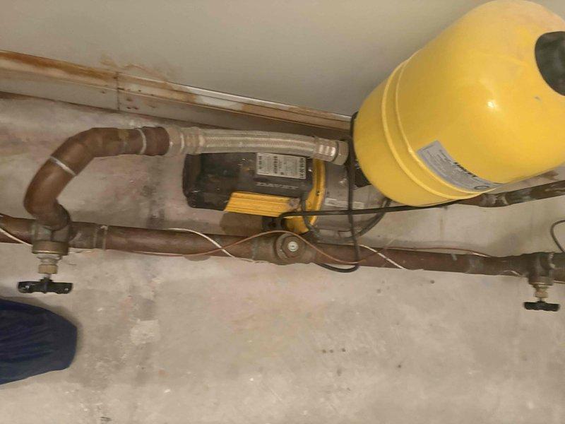 Responded to customer complaint of low water pressure throughout entire building. Upon investigation, inspected the overhead-mounted hydronic system including expansion tank, circulator pump, and associated piping network. Examined the yellow expansion tank with pressure valve, circulation pump unit, and copper distribution piping showing signs of oxidation and age-related discoloration. Assessed all visible components including shutoff valves, flexible connectors, and mounting hardware. Photographed system configuration for documentation purposes. Identified potential issues with the pressurization system that could be affecting water delivery throughout the building. System components appeared functional but showed normal operational wear consistent with age of installation.