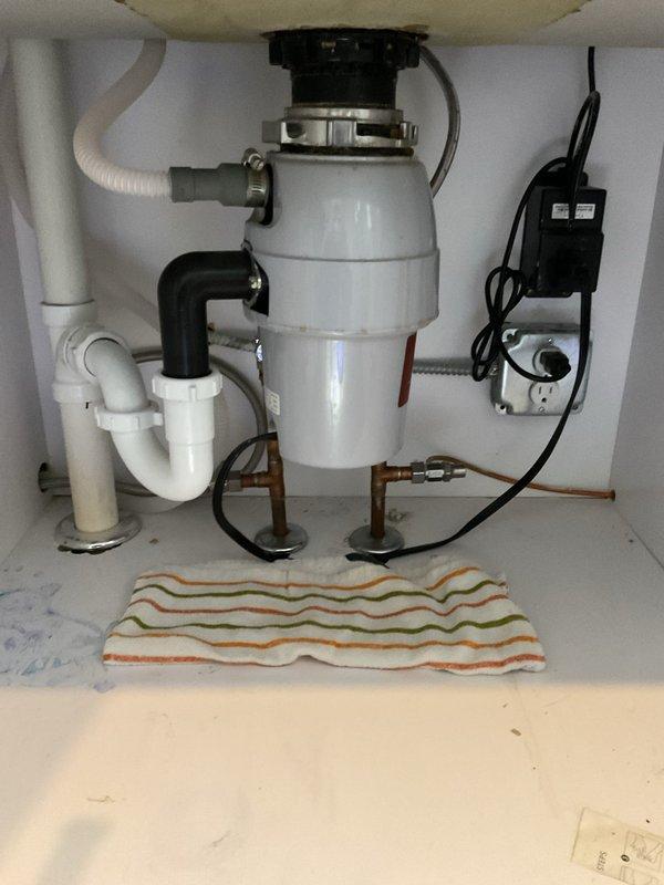 Responded to service call for leaking connection between kitchen sink and garbage disposal unit. Upon inspection, identified compromised seal at disposal mounting flange where unit connects to sink drain. Disassembled mounting assembly, cleaned mating surfaces, replaced worn rubber gasket and fiber gasket at flange connection, and reinstalled disposal unit with proper torque on mounting ring. Tested system under full water flow to verify leak was resolved and all connections remained dry.
