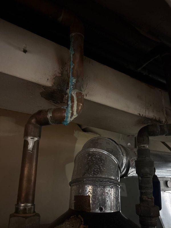 Responded to service call for pilot light that would not remain lit on tanked water heater. Upon arrival, found unit located in basement utility area with significant debris accumulation on top of tank and visible corrosion on copper supply piping. Inspected burner assembly and thermocouple, identifying failed thermocouple as primary cause of pilot outage. Observed blue-green copper corrosion deposits on vertical supply lines indicating prolonged moisture exposure and potential slow leak at connection points. Cleaned debris from tank top to ensure proper ventilation and prevent potential flue obstruction. Replaced faulty thermocouple with new OEM component and tested pilot ignition system for proper flame retention. Verified all gas connections for leaks using approved detection solution. Tightened corroded pipe fittings at elbow joint to address minor seepage. Tested unit through multiple heating cycles to confirm pilot stability and burner operation. Advised customer of aging infrast