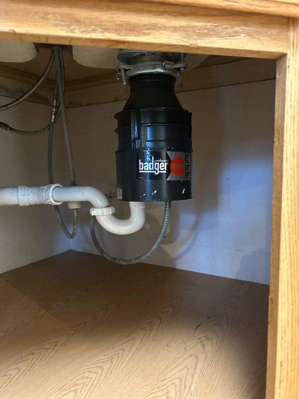 Responded to service call at rental property to repair garbage disposal unit. Upon inspection, found existing Badger model disposal unit mounted beneath kitchen sink with standard PVC drain configuration and electrical connection. Assessed unit operation, verified proper mounting hardware and plumbing connections, and ensured disposal was functioning correctly. Confirmed P-trap assembly and drain hose connections were secure with no leaks present. Unit tested successfully and left in proper working condition.
