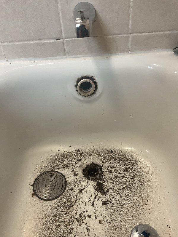 Responded to service call for bathtub draining extremely slow. Upon inspection, discovered significant accumulation of debris, dirt, and grime around the drain and basin area. Accessed plumbing system beneath the fixture, cleared obstruction from drainage line, and verified proper flow through the green PVC vertical stack and connected white PVC piping. Drainage restored to normal function and system tested successfully.
