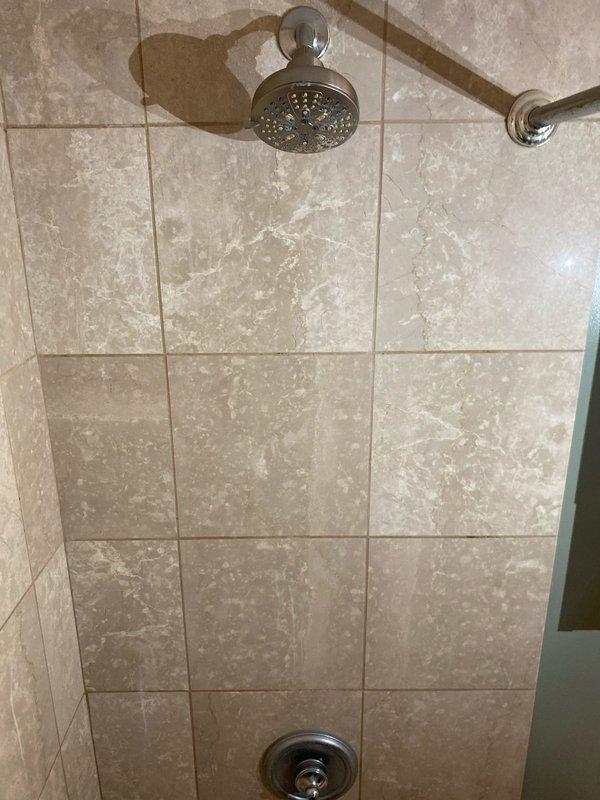 Responded to water leak complaint originating from upper unit bathroom and affecting the unit below. Upon arrival, inspected the bathroom and identified visible ceiling damage with peeling paint and surface deterioration in the lower unit, indicating active water intrusion. Examined the shower area in the upper unit, focusing on the tile surround, grout lines, shower fixtures, and wall penetrations. Documented water-damaged ceiling showing multiple areas of paint failure and underlying material exposure. Assessed shower enclosure with beige marble-pattern tile, chrome fixtures including rain showerhead, grab bar, and mixing valve for potential leak sources. Photographed evidence of damage for documentation purposes and to establish scope of issue for necessary repairs.