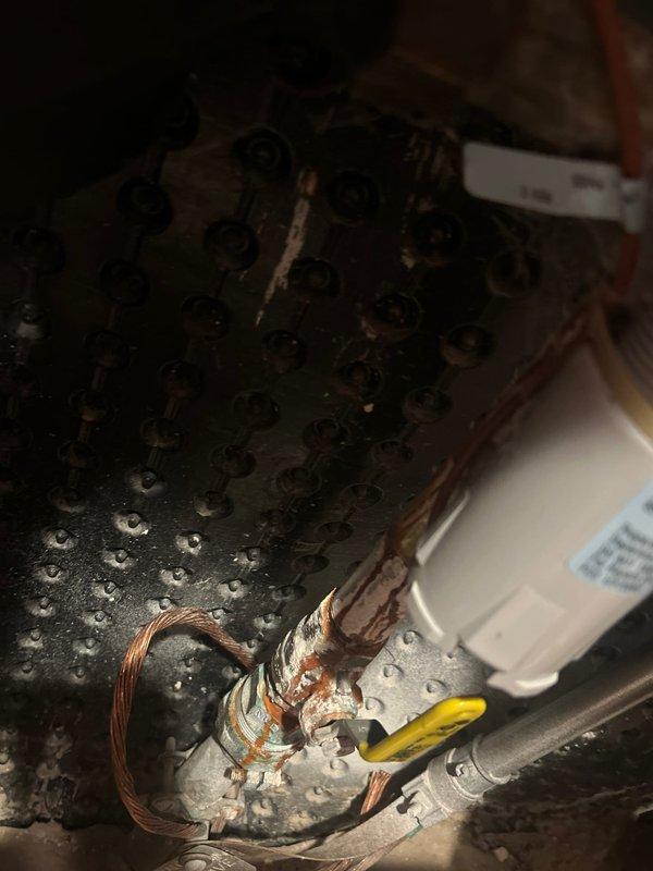 Responded to service call for outdoor water spigot inspection and assessment. Upon arrival, discovered severely corroded and deteriorated electrical wiring within associated mechanical system housing, with exposed copper conductors showing extensive oxidation and complete insulation failure in multiple areas. Documented hazardous wiring condition in humid environment with visible moisture present. Inspected exterior-mounted red hose bib installed through vinyl siding above stone veneer foundation, confirmed proper mounting and accessibility. Photographed all findings for service documentation and recommended immediate electrical repairs to address safety concerns with degraded wiring before further system operation.