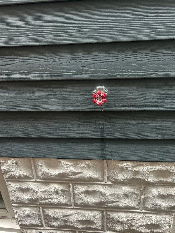 Responded to service call for outdoor water spigot inspection and assessment. Upon arrival, discovered severely corroded and deteriorated electrical wiring within associated mechanical system housing, with exposed copper conductors showing extensive oxidation and complete insulation failure in multiple areas. Documented hazardous wiring condition in humid environment with visible moisture present. Inspected exterior-mounted red hose bib installed through vinyl siding above stone veneer foundation, confirmed proper mounting and accessibility. Photographed all findings for service documentation and recommended immediate electrical repairs to address safety concerns with degraded wiring before further system operation.