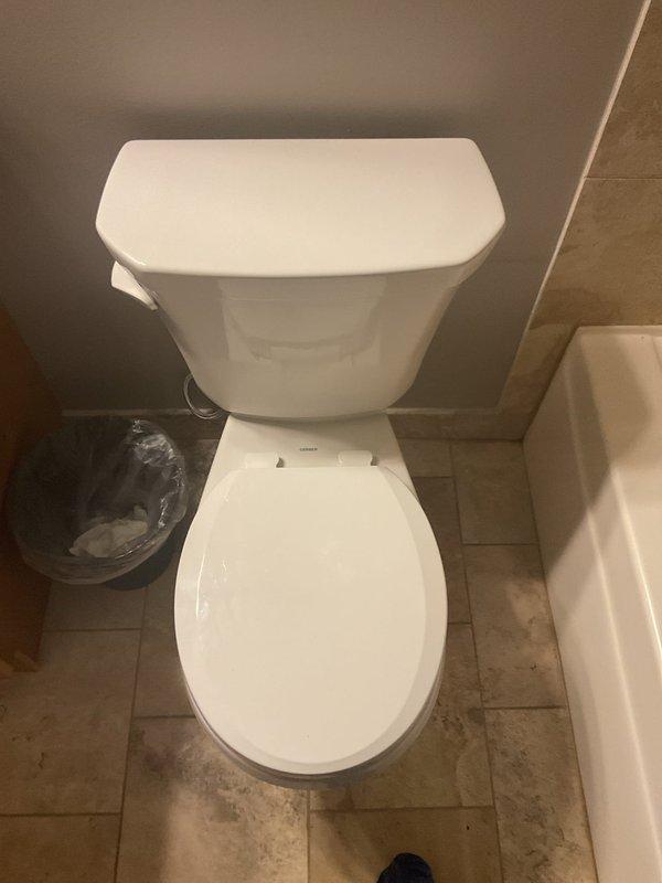 Completed toilet installation on third floor requiring two-person crew due to access and material handling requirements. Removed existing toilet fixture and assessed floor flange condition. Installed new two-piece white porcelain toilet with proper wax ring seal and mounting hardware, ensuring level placement and secure anchoring to floor flange. Reconnected water supply line and tested for proper fill, flush operation, and verified no leaks at base or supply connection. Floor drain visible in work area showed signs of previous moisture exposure with staining on surrounding tile, though not related to current installation scope. New toilet positioned against tiled wall with adequate clearance for operation and maintenance access. All components functioning properly upon completion with no water leakage detected during final inspection.