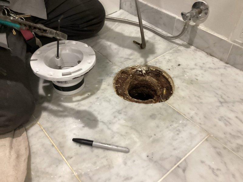 Responded to service call for floor drain inspection and maintenance. Upon arrival, found heavily corroded and deteriorated floor drain assembly in marble-tiled shower area with significant rust staining and oxidation around the drain flange and interior components. Removed existing drain cover and strainer assembly to assess condition of drain body and surrounding fixture. Documented extent of corrosion damage affecting the metal drain components. Evaluated drain opening integrity and water flow capacity to determine if replacement parts or complete drain assembly replacement would be required to restore proper function and prevent future leaks or drainage issues.