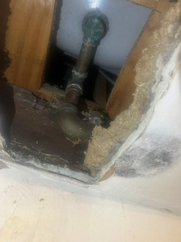 Responded to water leak investigation in basement laundry room where active leak from ceiling had caused significant structural damage. Located source of leak at corroded copper plumbing line within wall cavity above damaged area, evidenced by green patina oxidation on pipe and spherical valve assembly. Documented extensive ceiling and drywall deterioration with water staining, exposed wall cavity, and compromised building materials requiring immediate repair to prevent further damage.
