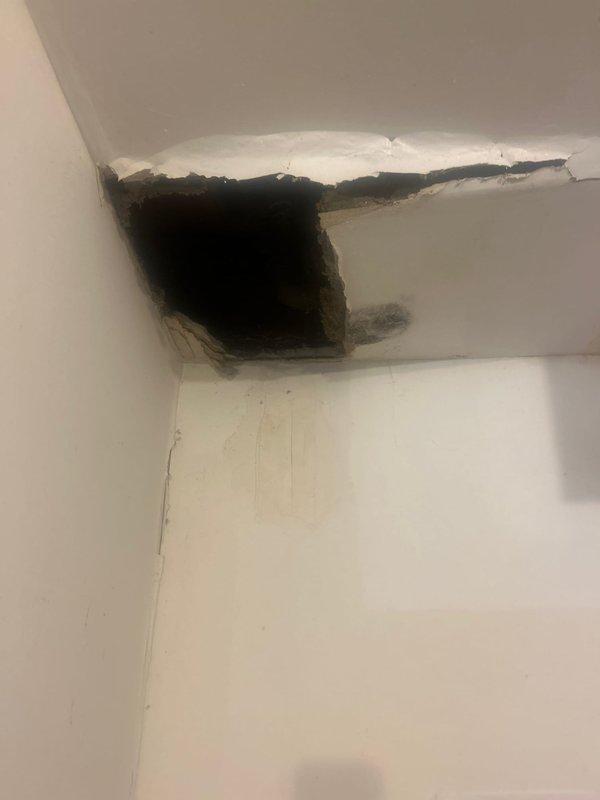 Responded to water leak investigation in basement laundry room where active leak from ceiling had caused significant structural damage. Located source of leak at corroded copper plumbing line within wall cavity above damaged area, evidenced by green patina oxidation on pipe and spherical valve assembly. Documented extensive ceiling and drywall deterioration with water staining, exposed wall cavity, and compromised building materials requiring immediate repair to prevent further damage.
