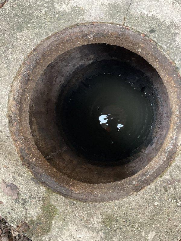 Responded to clogged drain service call and performed rodding operation from catch basin to main sewer line. Accessed the outdoor drainage system through concrete-mounted manhole opening, which showed standing water and significant corrosion on metal components. Utilized specialized drain cleaning equipment and long-handled rodding tools to clear blockage between catch basin and sewer connection. Customer advised that camera inspection video will be required to assess line condition and identify any underlying issues with the drainage system.