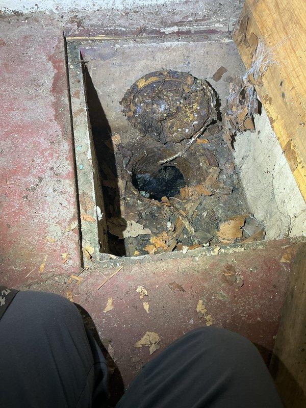 Completed callback to inspect and photograph existing sump pump system and deteriorated flooring conditions. Documented corroded floor drain assembly with exposed subfloor damage and significant water staining on concrete basement floor surrounding sump pit. Observed functional sump pump installation with PVC discharge piping and check valve in place, though extensive floor deterioration and rust patterns indicate previous water intrusion issues requiring attention.