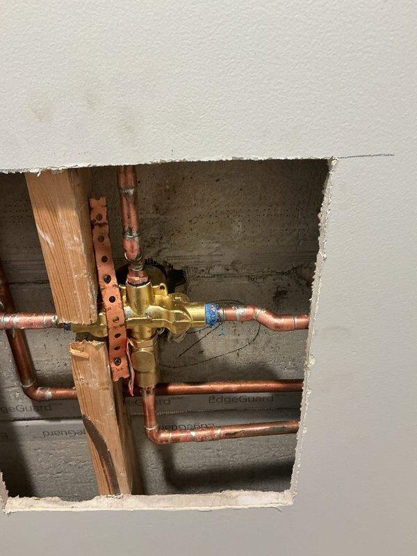 Performed warranty service on shower valve system. Accessed plumbing assembly through wall opening to expose brass mixing valve with multiple copper supply line connections. Removed and replaced defective HAIN-YO indexed cartridge assembly dated 01/22/25, including associated brass fittings and hardware. Verified proper hot and cold water operation through valve body and confirmed all connections were secure prior to reassembly.