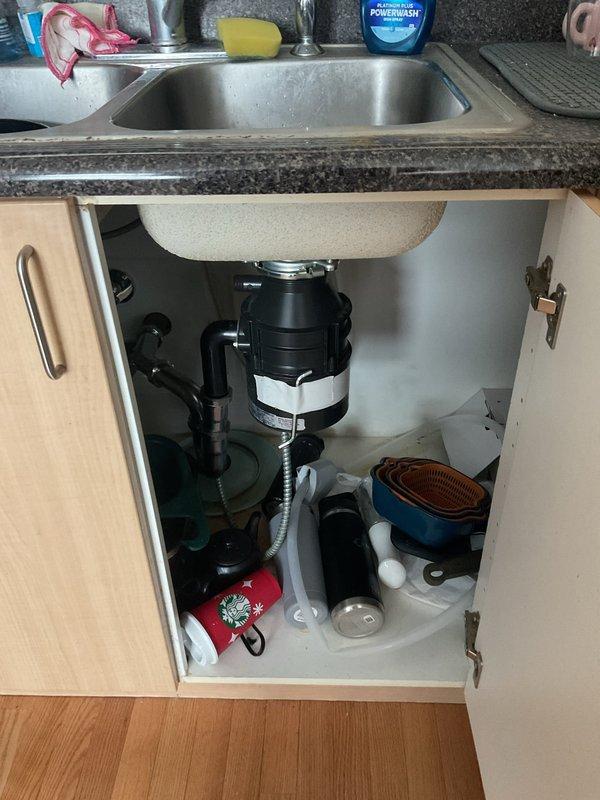 Responded to service call regarding excessive noise from recently installed garbage disposal unit. Upon inspection, diagnosed potential clog in disposal system. Examined under-sink plumbing configuration including black garbage disposal unit, drainage connections, and corrugated discharge hose. Assessed drain assembly and verified proper installation of disposal mounting and connections to double-basin stainless steel sink system.