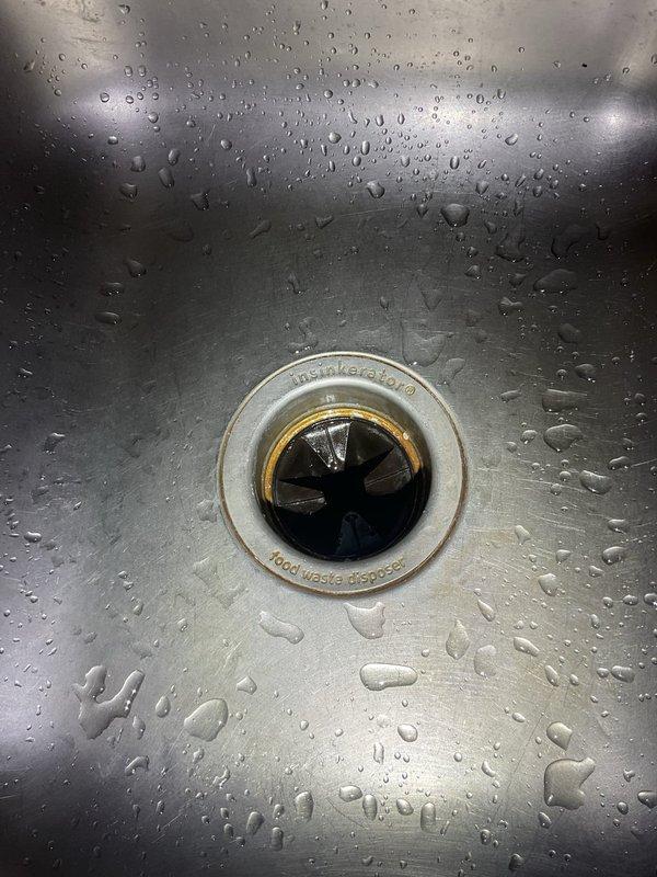 Responded to service call regarding excessive noise from recently installed garbage disposal unit. Upon inspection, diagnosed potential clog in disposal system. Examined under-sink plumbing configuration including black garbage disposal unit, drainage connections, and corrugated discharge hose. Assessed drain assembly and verified proper installation of disposal mounting and connections to double-basin stainless steel sink system.