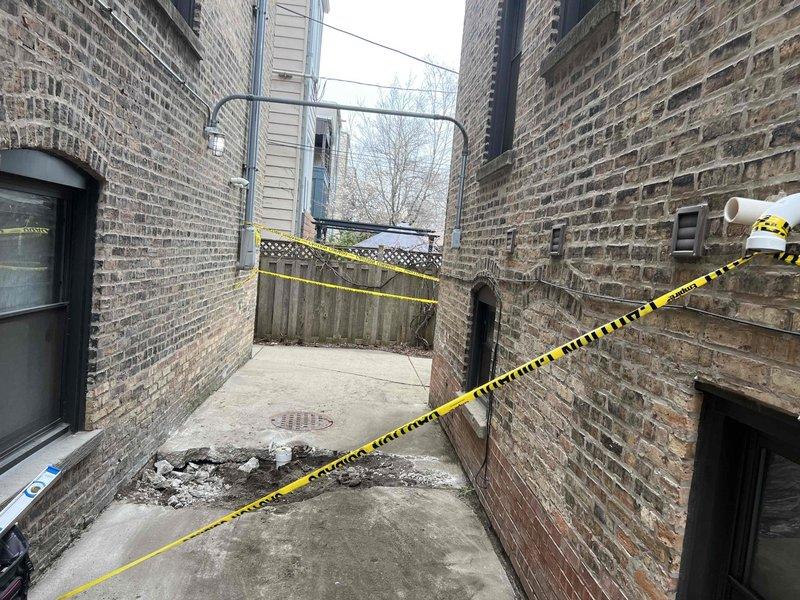 Assessed exterior drainage issue in alleyway between buildings where significant water pooling was observed on concrete surface near brick structures. Identified failed or inadequate drainage system causing water accumulation despite presence of existing drain infrastructure. Area was cordoned off with caution tape for safety due to standing water hazard. Documented conditions showing water collection on ground surface with nearby circular drain cover that was not effectively managing water flow. Repair has been sold and awaiting parts arrival to complete drainage system repair work.