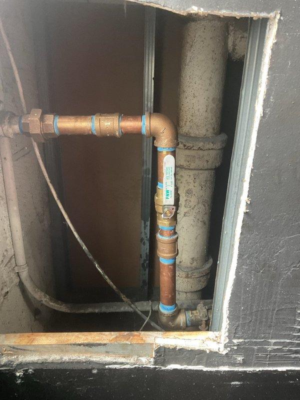 Coordinated building shutdown from 10AM-2PM to complete sold plumbing repair work. Accessed plumbing infrastructure through wall opening to service copper piping with multiple connection points, including elbow joints and vertical runs marked with blue identification bands. Completed necessary repairs to the plumbing system within the scheduled shutdown window, ensuring minimal disruption to building operations.
