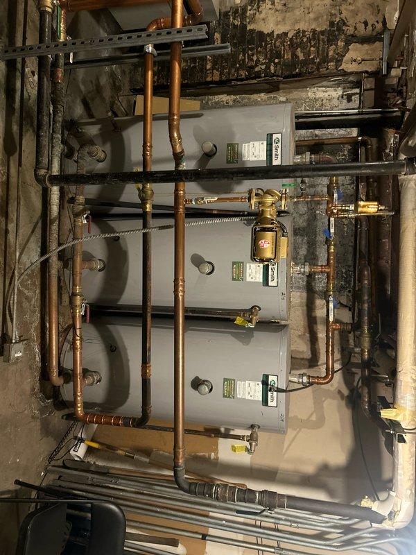 Conducted comprehensive assessment of building water pressure system in response to complaints from upper-floor units regarding insufficient water pressure. Evaluated existing return pump and booster pump systems, inspecting three stacked water heater units with interconnected copper piping network, multiple brass valves, and pressure relief components. Examined mechanical room infrastructure including blue-colored pumping equipment with valve assemblies, insulated vertical piping columns with copper distribution lines, and overall system configuration to identify deficiencies affecting water delivery to upper floors and provide recommendations for corrective actions to restore adequate pressure throughout the building.