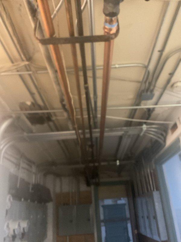 Performed plumbing repair work requiring building water shutdown during scheduled four-hour service window. Created ceiling access opening to reach overhead plumbing infrastructure, exposing floor joists to access multiple water supply lines including copper piping and PVC drain lines. Completed necessary repairs to piping system, with all lines properly secured using metal straps and hangers per code requirements.