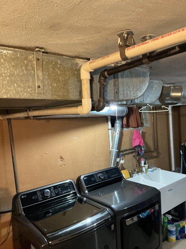Responded to a clogged upstairs drain that was identified during routine HVAC maintenance by another contractor. Upon arrival, inspected the plumbing system in the utility area where washing machines and laundry fixtures are located. Assessed the drainage issue and documented the existing plumbing configuration, including exposed PVC drain lines and connections in the mechanical/laundry room area.