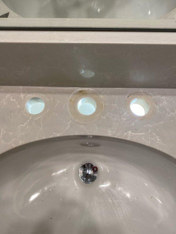 Replaced existing bathroom faucet assembly with new three-piece chrome fixture including center spout and dual lever handles. Removed old faucet showing discoloration and staining around mounting holes, cleaned sink deck surface, and installed new fixture ensuring proper water flow and leak-free connections as verified during testing.