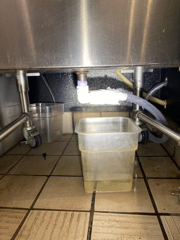 Responded to priority service call for leaking ice bin drain system. Upon inspection, found deteriorated drain hose failing to properly convey discharge to floor drain, resulting in water accumulation beneath commercial ice bin unit. Documented existing conditions showing compromised flexible drain line and liquid collecting in temporary catch basin on floor. Provided estimate for replacement of drain hose assembly with properly sized flexible line to ensure adequate reach and secure connection to floor drain, eliminating leak condition and restoring proper drainage function.