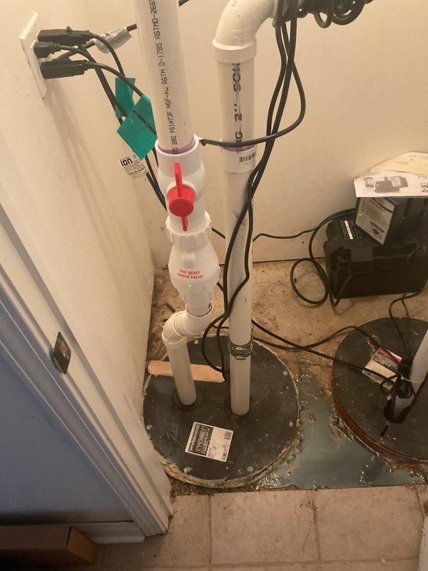 Responded to residential sewer repair call for malfunctioning sump pit ejector pump system. Upon inspection, evaluated the existing PVC piping configuration, ejector pump assembly, and associated electrical controls in the utility area. The system included vertical discharge piping with check valve and shut-off valve arrangements connected to the ejector pump basin. Documented the current installation showing white PVC discharge lines, red-handled gate valve, check valve assembly, and control box with wiring connections. Assessed the pump operation, electrical connections, and plumbing configuration to diagnose the reported ejector pump issue and provided estimate for necessary repairs to restore proper wastewater discharge functionality.