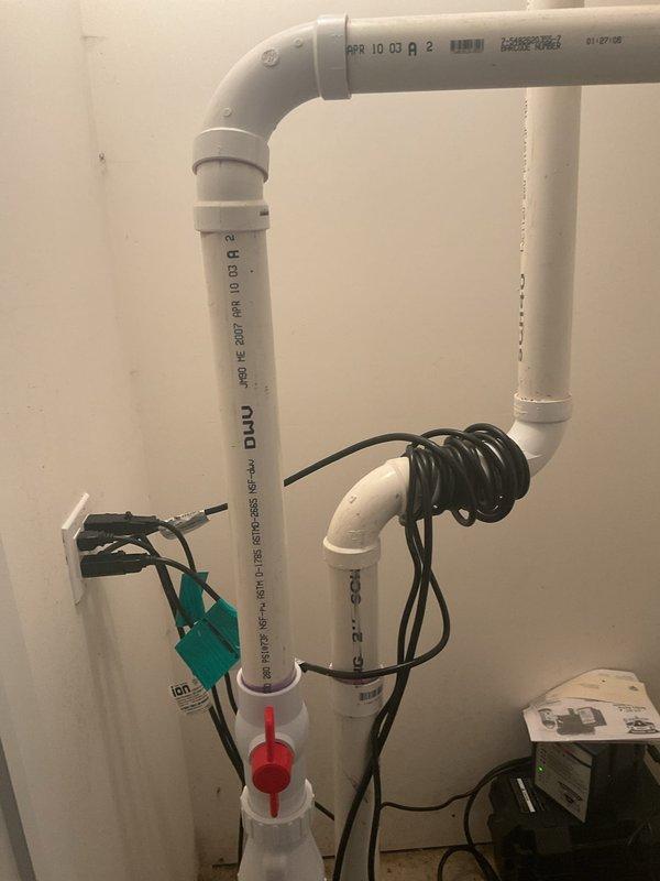 Responded to residential sewer repair call for malfunctioning sump pit ejector pump system. Upon inspection, evaluated the existing PVC piping configuration, ejector pump assembly, and associated electrical controls in the utility area. The system included vertical discharge piping with check valve and shut-off valve arrangements connected to the ejector pump basin. Documented the current installation showing white PVC discharge lines, red-handled gate valve, check valve assembly, and control box with wiring connections. Assessed the pump operation, electrical connections, and plumbing configuration to diagnose the reported ejector pump issue and provided estimate for necessary repairs to restore proper wastewater discharge functionality.