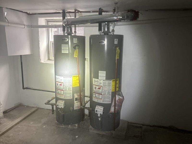 Conducted on-site evaluation of dual water heater system and exterior drainage concern. Inspected two residential water heaters located in basement utility room, documenting current condition, piping connections, and installation configuration. Both units assessed for age, capacity, operational status, and compliance with current plumbing codes. Examined water supply lines, pressure relief valves, venting system, and gas or electric connections as applicable.

Investigated reported exterior drainage issue by inspecting concrete drainage enclosure with center floor drain. Documented debris accumulation consisting of leaves and organic matter along perimeter and in corners that may be impeding proper water flow. Assessed concrete surfaces for cracks, deterioration, or settling that could contribute to drainage problems. Evaluated drain cover condition and verified accessibility for maintenance. Photographed all findings to support estimate preparation for water heater replacement options