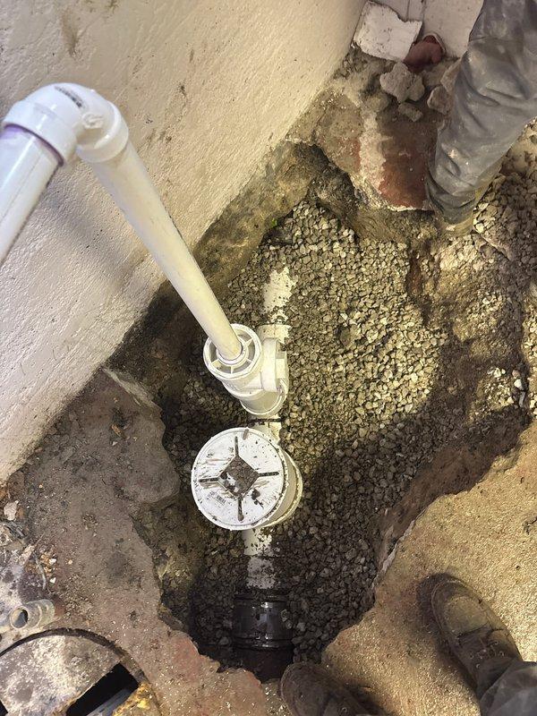 Completed excavation and installation of PVC drainage system in below-grade access pit. Removed deteriorated plumbing components and replaced with new white PVC pipe assembly including elbow joints, cleanout access port, and proper fittings. Addressed standing water issue at pit base and ensured proper drainage flow. Installed circular drain cover at surface level with appropriate connections to existing infrastructure. All connections secured and tested for proper function.