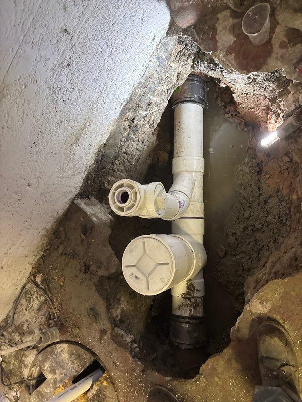 Completed excavation and installation of PVC drainage system in below-grade access pit. Removed deteriorated plumbing components and replaced with new white PVC pipe assembly including elbow joints, cleanout access port, and proper fittings. Addressed standing water issue at pit base and ensured proper drainage flow. Installed circular drain cover at surface level with appropriate connections to existing infrastructure. All connections secured and tested for proper function.