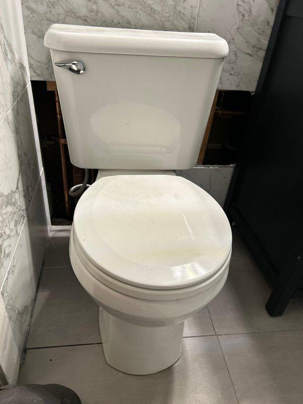 Completed commercial plumbing repair involving copper piping installation and toilet fixture work. Installed parallel copper water supply lines with proper fittings and joints in exposed wall cavity between structural framing members. Set and secured standard two-piece toilet fixture on gray tile flooring against marble-patterned wall tile, with chrome flush lever properly mounted and operational.
