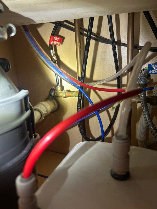 Responded to service call for reported water heater leak located under sink. Upon arrival, performed thorough inspection of under-sink plumbing assembly including water heater connections, supply lines, shut-off valves, and associated flex hoses. Examined brass fittings, braided stainless steel flexible connectors, and corrugated hot and cold water supply lines for signs of moisture, corrosion, or active leaking. Inspected connection points between water heater unit and distribution system, verifying integrity of all compression fittings and threaded connections. Documented existing plumbing configuration with photographic evidence showing complete under-cabinet assembly including shut-off valves with identification tags, multiple flexible supply lines, and mounting hardware. Provided estimate for necessary repairs to resolve ongoing leak issue.