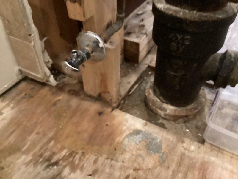 Responded to priority call for leaking toilet valve. Upon arrival, found chrome-plated shut-off valve actively leaking at the connection point in an unfinished utility area with exposed floor joists and rough plumbing. Placed collection container beneath the valve to contain water discharge and prevent further damage to subflooring. Assessed the condition of the copper supply line and valve assembly, noting signs of age and corrosion on surrounding plumbing components. Documented existing conditions including stained subflooring and exposed wall framing for reference. Valve required immediate attention to stop active leak and restore proper water control to the toilet fixture.
