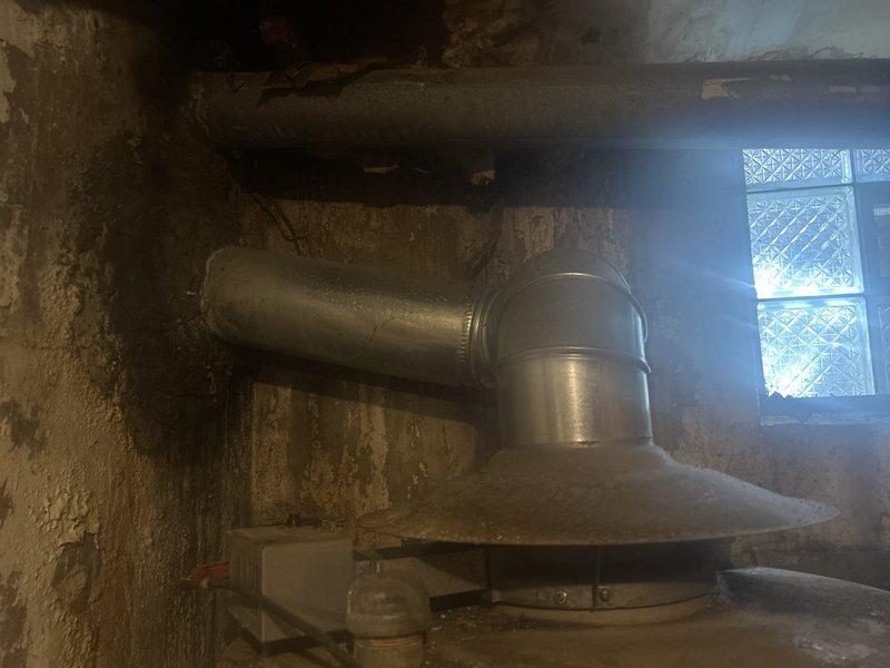 Conducted on-site assessment for 100-gallon water heater replacement in basement utility area. Evaluated existing unit showing signs of age and deterioration, documented current installation configuration including venting system with metallic exhaust hood and horizontal ductwork. Inspected surrounding infrastructure, concrete flooring conditions, and existing plumbing connections to determine replacement requirements and compatibility with new equipment installation.