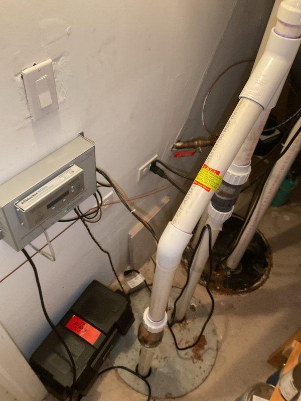 Responded to customer complaint of noisy sump pump operation in 20-year-old residential property. Upon arrival, conducted thorough inspection of sump pump system, discharge piping, and associated electrical components in basement utility area. Assessed pump motor, float switch mechanism, and check valve for proper operation and signs of wear. Examined PVC discharge lines, fittings, and connections for secure mounting and potential sources of vibration or water hammer. Verified electrical connections at control panel and pump unit were secure and functioning within normal parameters. Identified source of noise and provided customer with findings and recommendations for resolution. Documented system condition with photographic evidence showing plumbing configuration, electrical controls, and overall installation setup.