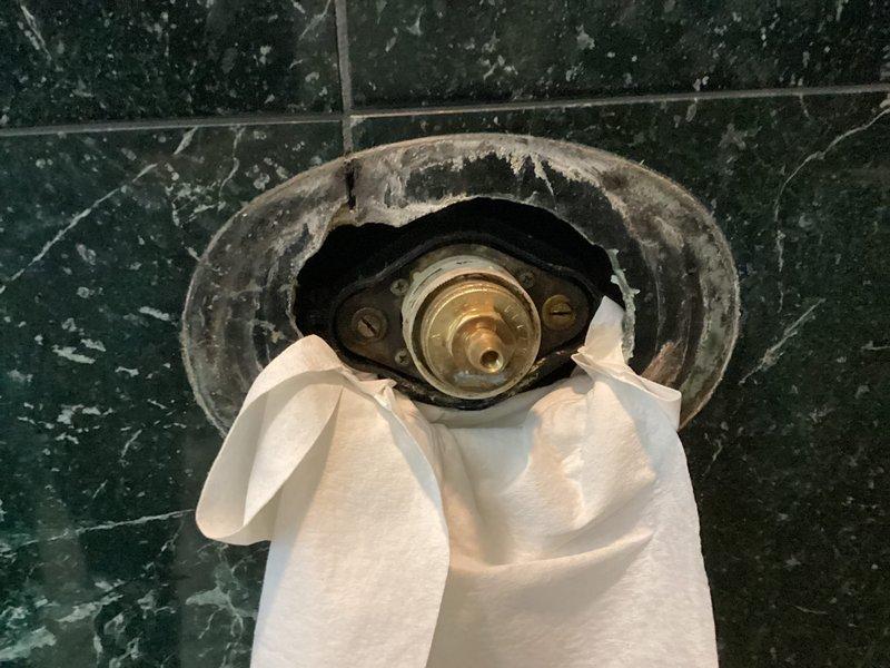 Completed shower valve replacement in bathroom with green marble tile surround. Removed corroded and deteriorated escutcheon plate and aging brass valve assembly that showed significant wear from water exposure. Cut access opening in adjacent wall to expose copper supply lines and shutoff valves. Installed new shower control valve with proper connections to existing copper piping. Repaired wall opening and restored finish. System tested and confirmed proper operation with no leaks.