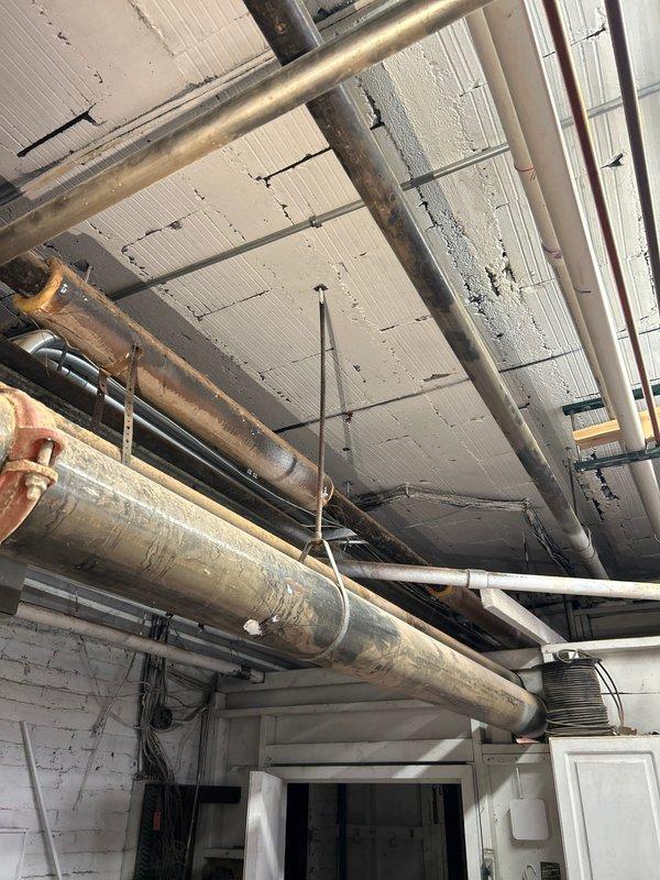 Responded to water leak complaint near laundry room area. Upon inspection, located source of slow leak in basement mechanical space affecting multiple corroded supply lines running along ceiling near laundry area. Extensive rust and oxidation observed throughout exposed piping system, indicating aged infrastructure with compromised integrity. Documented deteriorated pipe conditions showing heavy corrosion on horizontal runs, multiple elbow joints, and connecting fittings secured with metal hangers to ceiling structure.