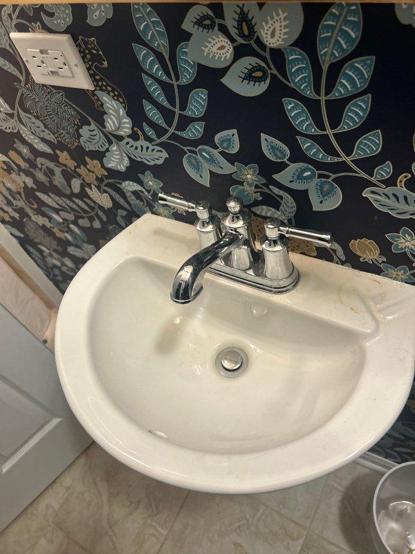 Installed new chrome two-handle faucet fixture on white pedestal sink in residential powder room. Replaced existing faucet with traditional-style unit featuring separate hot and cold water lever handles and curved spout, ensuring proper mounting, water supply connections, and leak-free operation upon completion.