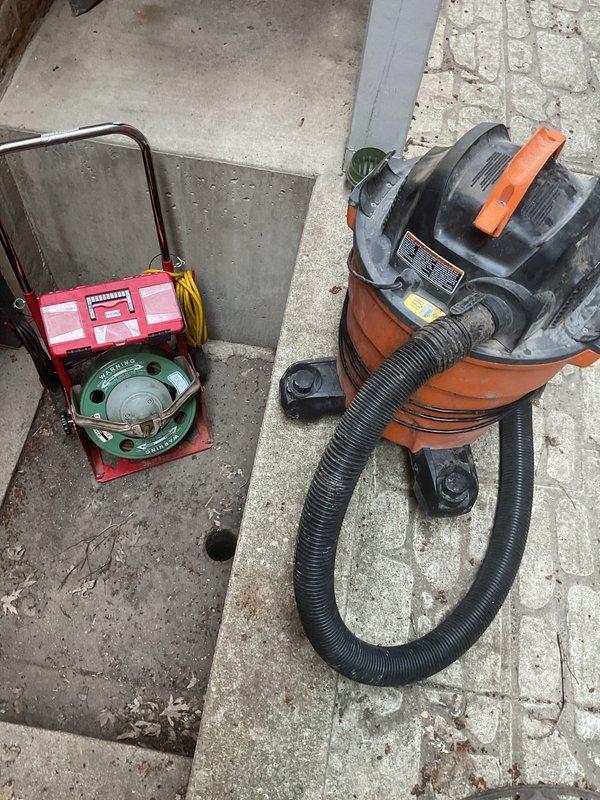 Responded to clogged outdoor drainage system. Upon arrival, found circular drain cover in concrete channel heavily obstructed with accumulated leaves, debris, and organic matter causing water backup. Deployed wet/dry vacuum equipment and specialized drain cleaning tools to remove blockage and restore proper water flow through the drainage system.