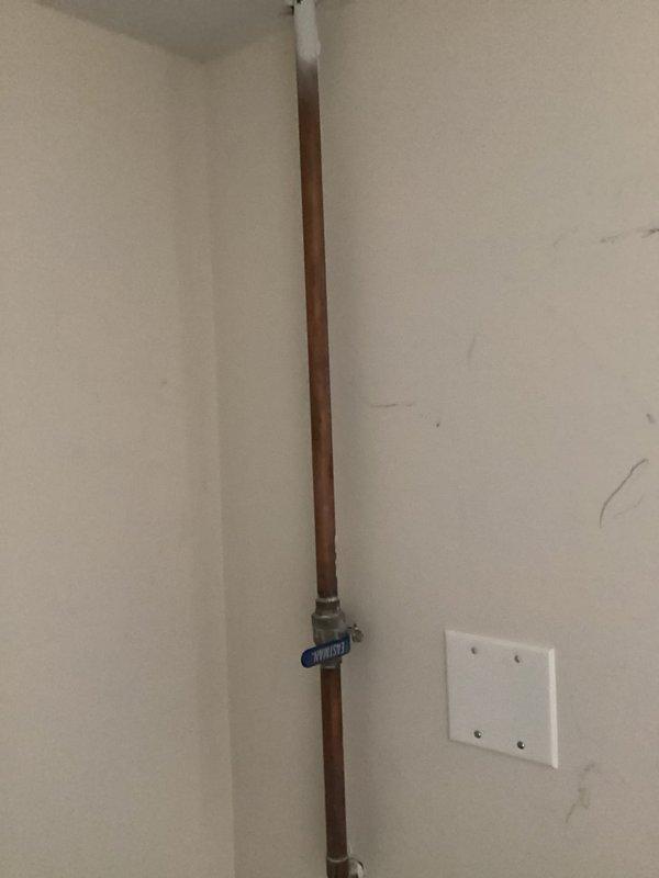 Responded to outdoor spigot backup issue where water was leaking into storage unit at the shut-off valve location. Inspected exterior hose bib mounted on white brick wall and traced supply line to interior copper piping with blue-handled shut-off valve in corner of storage area. Identified leak at valve connection point and resolved water intrusion issue to prevent further damage to storage space.