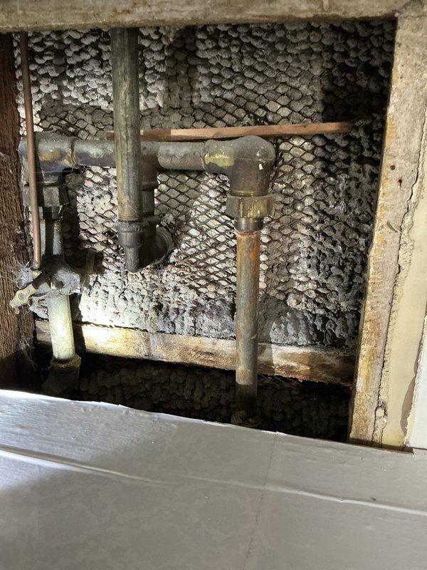Responded to low water pressure complaint and accessed built-in linen closet to inspect plumbing infrastructure behind wall panel. Upon investigation, discovered aged and corroded horizontal supply pipes with significant rust accumulation affecting water flow throughout the system. Documented deteriorated piping conditions showing oxidation and mineral buildup that was restricting water pressure to fixtures.