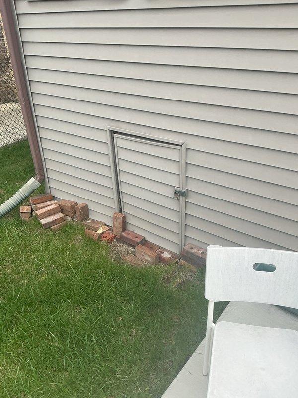 # Flood Control System Installation - Exterior Basement Stairwell

Completed residential drainage assessment and flood control installation for exterior basement stairwell entrance experiencing moisture accumulation and water drainage issues. The concrete stairwell, consisting of 5-6 weathered steps descending between wooden siding and brick walls, showed evidence of persistent water pooling at the landing area with debris accumulation and moisture damage.

Evaluated existing drainage infrastructure including white PVC pipe at landing and assessed water flow patterns contributing to flooding concerns. Documented deteriorated concrete surfaces and inadequate drainage capacity at the lower level entrance point. Recommended and prepared site for flood control system installation to redirect water away from basement access point and prevent future water intrusion. Inspected crawlspace ventilation access panels and surrounding grade conditions to ensure comprehensive drainage solution addre