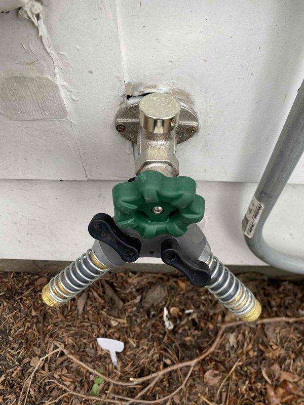 Responded to service call for water leak occurring at interior plumbing connection when outdoor spigot was activated. Upon inspection, identified leak at wall penetration point where supply line transitions from interior to exterior. Accessed leak location through interior wall opening, repaired faulty connection at pipe junction, and verified proper seal at wall penetration. Tested outdoor spigot assembly with Y-connector attachment under full water pressure to confirm leak was eliminated and all connections remained dry during operation.