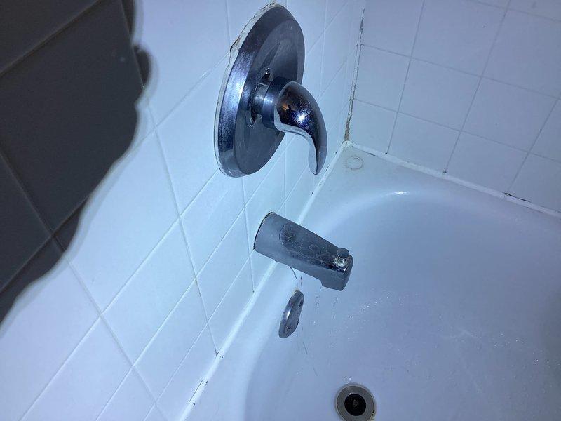 Responded to complaint of whistling noise from shower during water flow that had persisted for approximately two weeks. Upon inspection, examined the bathtub and shower fixture assembly, including the chrome faucet valve, tub spout with diverter, and associated plumbing connections. Identified that the whistling sound was likely caused by restricted water flow through a partially obstructed valve seat or worn internal components within the aging fixture assembly. Documented the condition of the 25-year-old plumbing system, noting visible signs of fixture wear, mineral deposits, and deteriorated caulking around escutcheon plates and wall penetrations. Photographed the existing chrome fixtures mounted on white tile surround for service records, capturing both the faucet valve assembly and tub spout configuration to document current installation and condition prior to any recommended repairs or replacements.