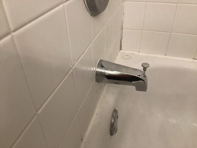 Responded to complaint of whistling noise from shower during water flow that had persisted for approximately two weeks. Upon inspection, examined the bathtub and shower fixture assembly, including the chrome faucet valve, tub spout with diverter, and associated plumbing connections. Identified that the whistling sound was likely caused by restricted water flow through a partially obstructed valve seat or worn internal components within the aging fixture assembly. Documented the condition of the 25-year-old plumbing system, noting visible signs of fixture wear, mineral deposits, and deteriorated caulking around escutcheon plates and wall penetrations. Photographed the existing chrome fixtures mounted on white tile surround for service records, capturing both the faucet valve assembly and tub spout configuration to document current installation and condition prior to any recommended repairs or replacements.