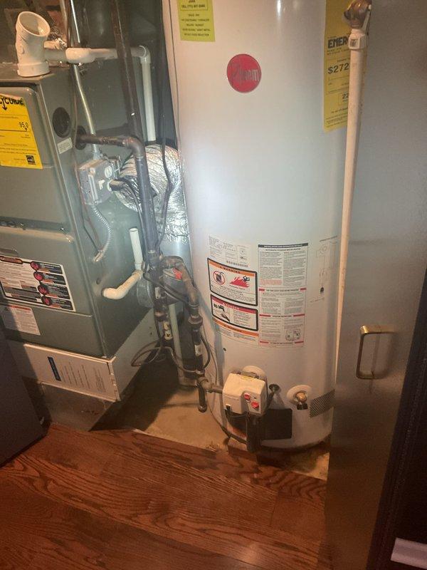 Completed water heater replacement in residential utility room. Removed existing unit and installed new white cylindrical water heater with proper venting, pressure relief valve, drain pan assembly, and all required connections to existing plumbing and HVAC systems. All manufacturer specifications, Energy Guide labels, and safety warnings properly affixed and equipment tested for normal operation.