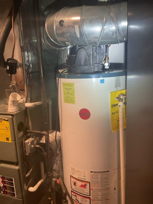 Completed water heater replacement in residential utility room. Removed existing unit and installed new white cylindrical water heater with proper venting, pressure relief valve, drain pan assembly, and all required connections to existing plumbing and HVAC systems. All manufacturer specifications, Energy Guide labels, and safety warnings properly affixed and equipment tested for normal operation.