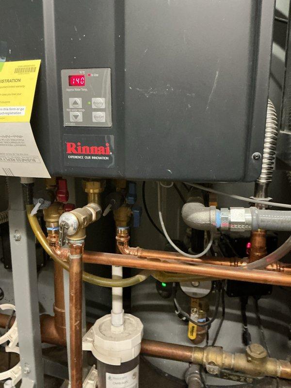 Responded to emergency service call for leaking Rinnai tankless water heater. Upon arrival, inspected unit and associated plumbing connections including copper supply lines, brass fittings, and shut-off valves. Documented existing installation configuration showing unit mounted with digital display operational at 148°F, along with connected expansion tank and filtration system. Assessed mechanical room environment containing multiple heating units and venting infrastructure to determine source of leak and appropriate repair approach.