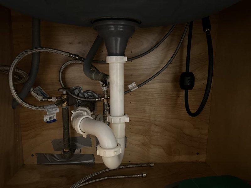 Completed faucet installation in kitchen with verification of proper water supply connections via braided stainless steel flex lines and functional drain assembly including garbage disposal unit. Assessed existing galvanized supply piping for potential future repiping needs due to age and condition of visible plumbing infrastructure.