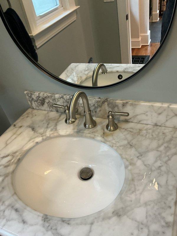 Replaced bathroom faucet with customer-supplied brushed nickel widespread three-piece faucet set on marble vanity countertop. Removed existing fixture, installed new widespread faucet assembly with central spout and dual handle controls, connected braided stainless steel supply lines to existing shut-off valves, and verified proper water flow and drainage with no leaks detected.