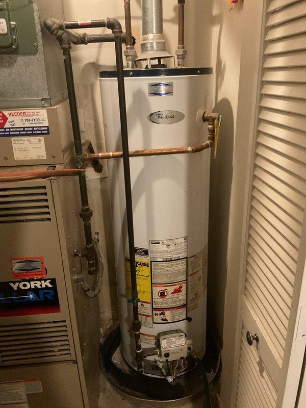 Completed on-site assessment of residential water heating system due to loss of hot water. Inspected existing white Whirlpool tank-style water heater located in utility room, noting all plumbing connections, gas supply lines, venting configuration, and seismic strapping. Documented shut-off valve locations including red and yellow handled valves on supply lines, copper piping connections, and metallic vent pipe with 90-degree elbow configuration. Evaluated clearances around unit in relation to adjacent York HVAC equipment and confirmed accessibility for replacement. Photographed current installation including all pipe routing, electrical connections visible via wall-mounted green panel, and proper seismic restraint strapping. Provided comprehensive estimate for complete water heater replacement including removal and disposal of existing unit, installation of new tank-style water heater with code-compliant connections, and all necessary materials and labor.